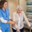 A professional caregiver helps an older client with a walker get around.