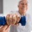 An older man is helped to lift a weight as part of physical therapy.