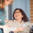 A happy home nurse helps a smiling patient in a wheelchair, representing how home health can help with pain management.